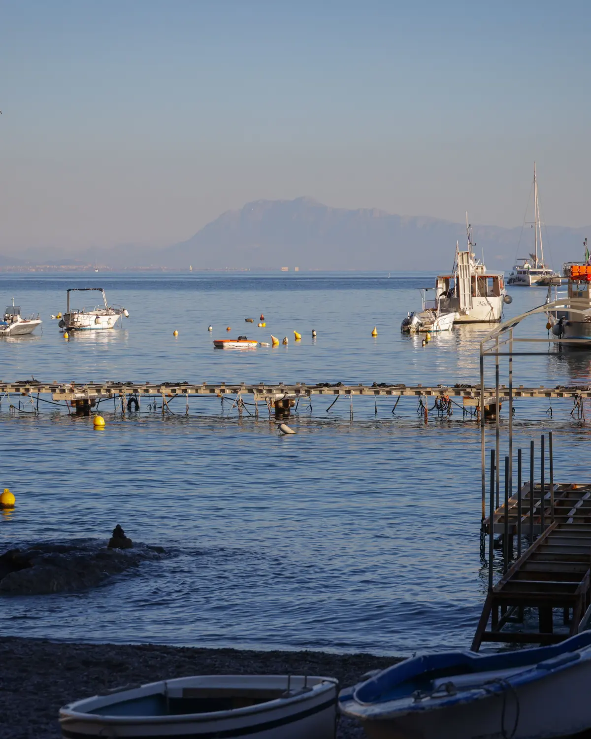 Small fishing boats moored off a shingle shore at first light with mountains across the water