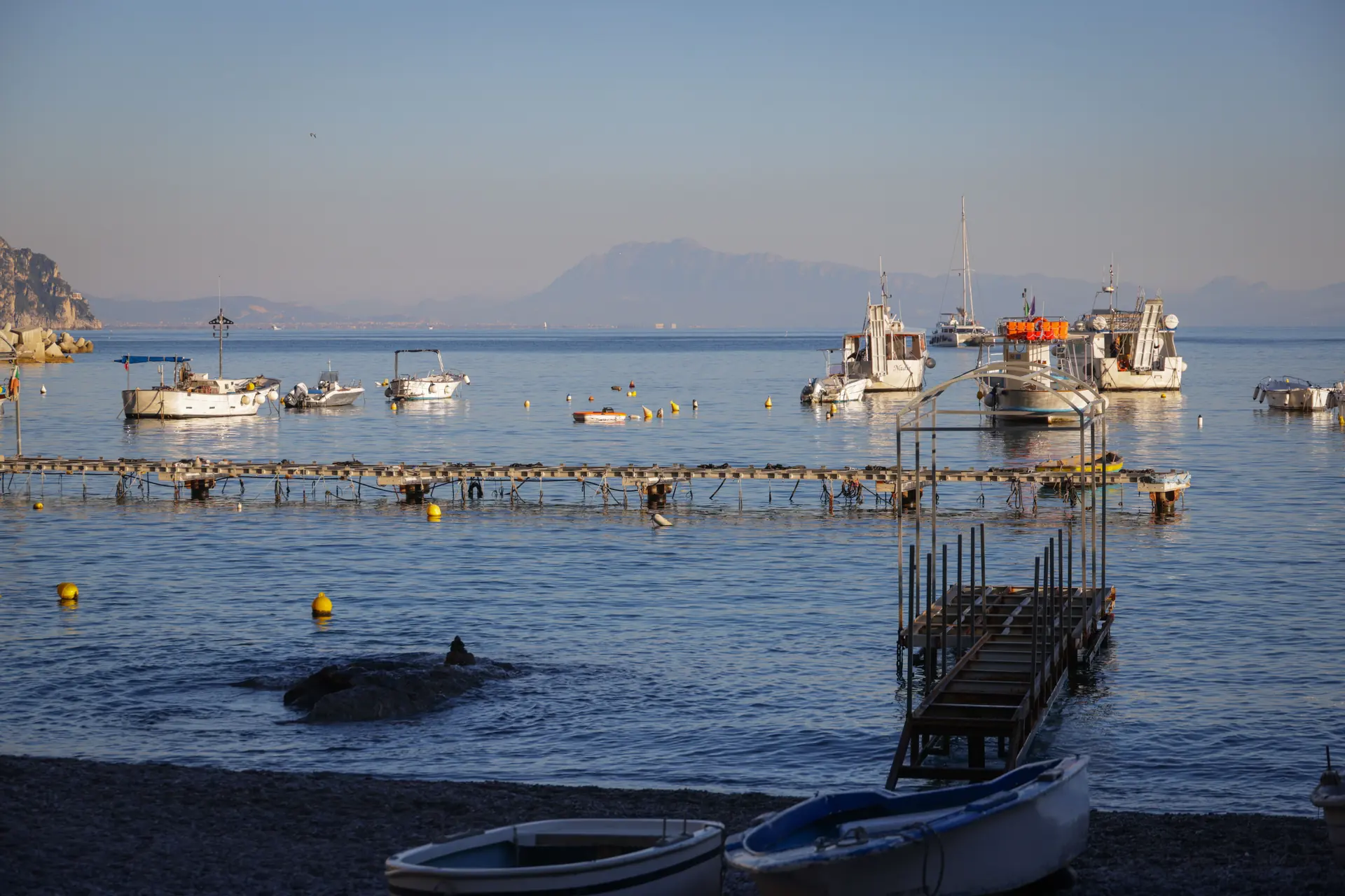 Small fishing boats moored off a shingle shore at first light with mountains across the water