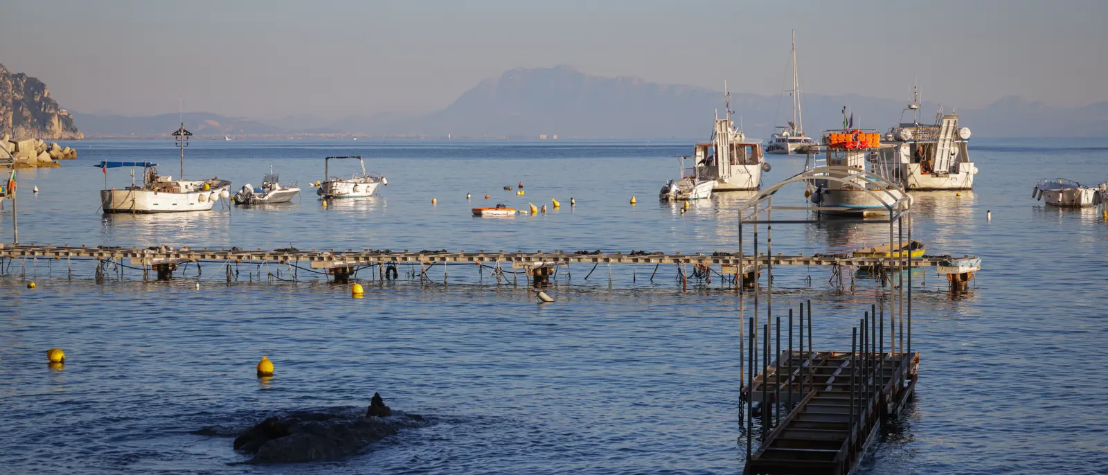 Small fishing boats moored off a shingle shore at first light with mountains across the water