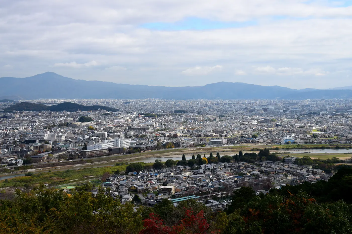 The low-rise Kyoto basin with grey tiled roofs and a braided river, closed by forested ridges in late autumn