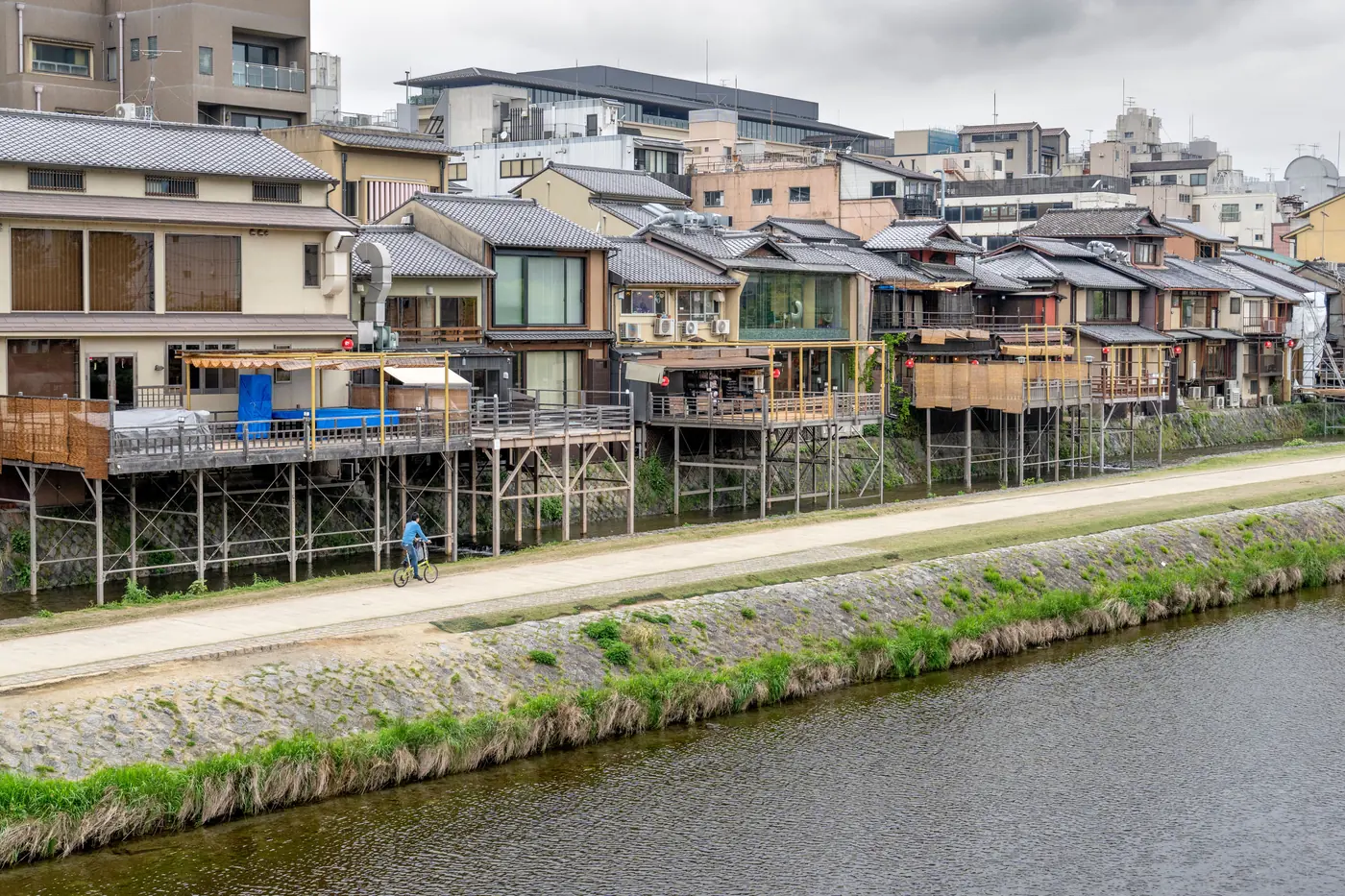 Timber riverside houses on tall stilts above the Kamo river in Kyoto under flat grey light