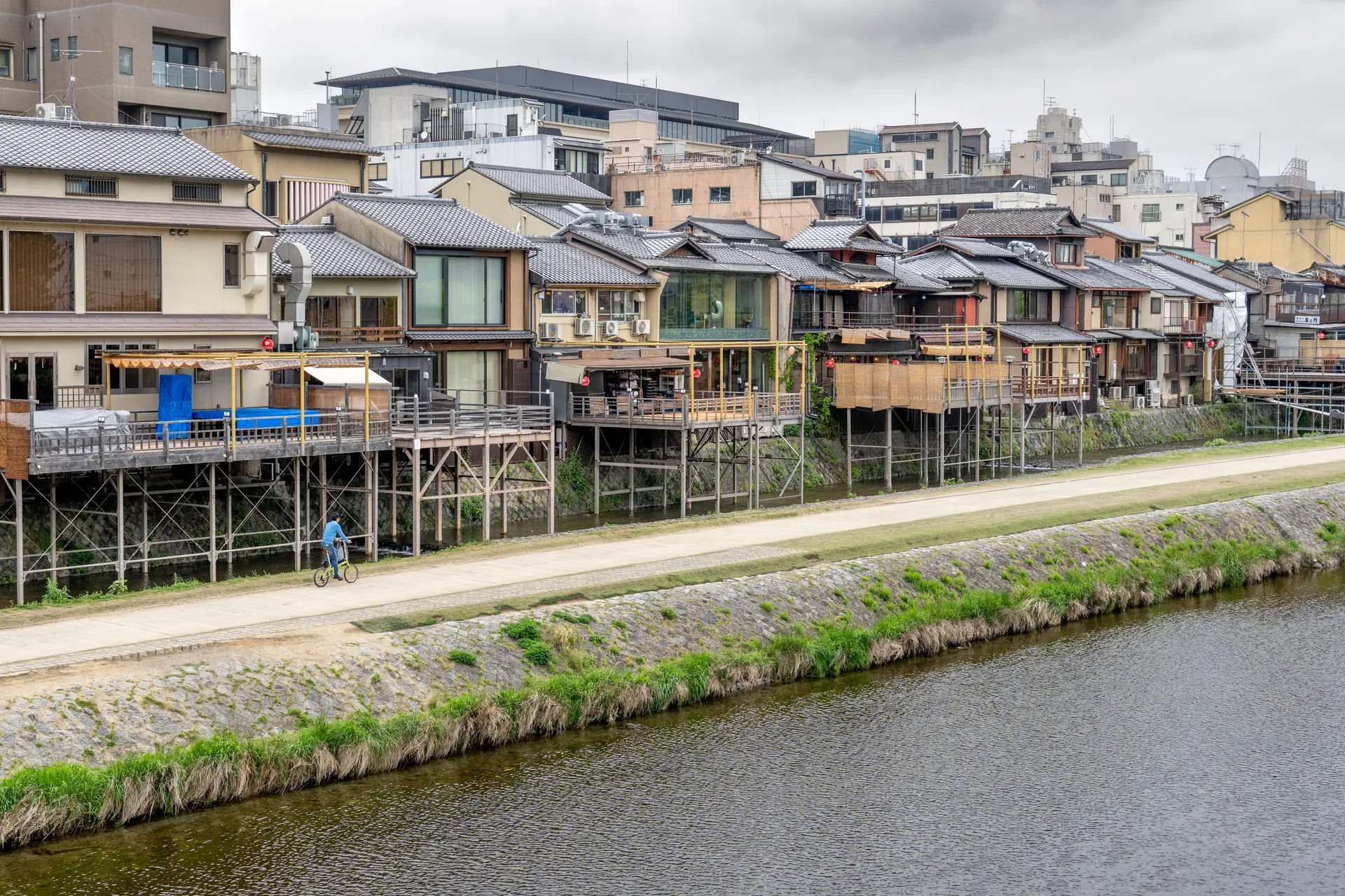 Timber riverside houses on tall stilts above the Kamo river in Kyoto under flat grey light