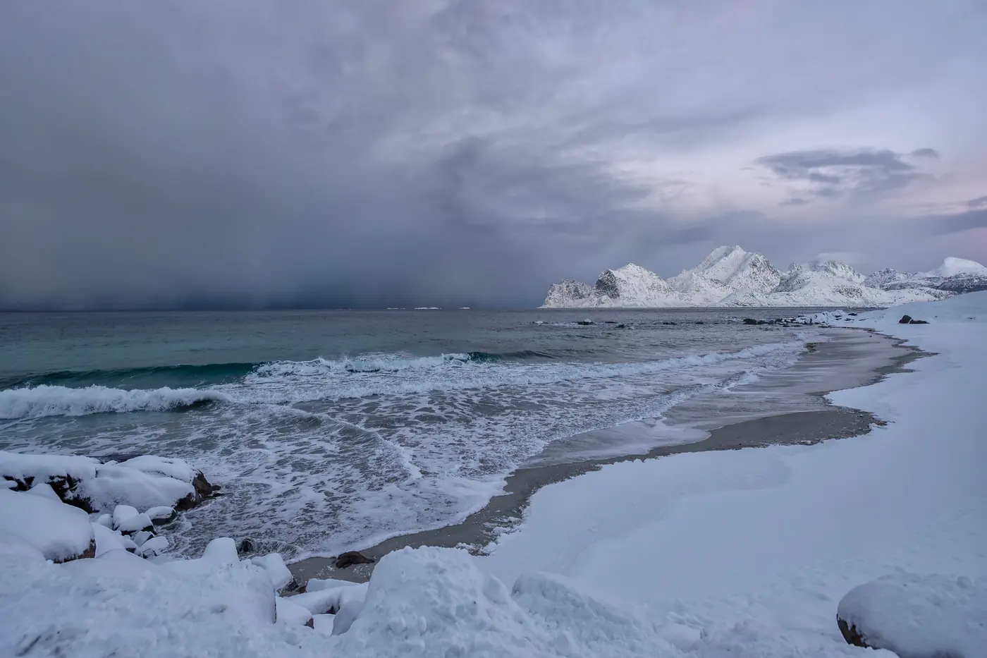 Snow lying to the tideline at Haukland beach in Lofoten with turquoise cold water