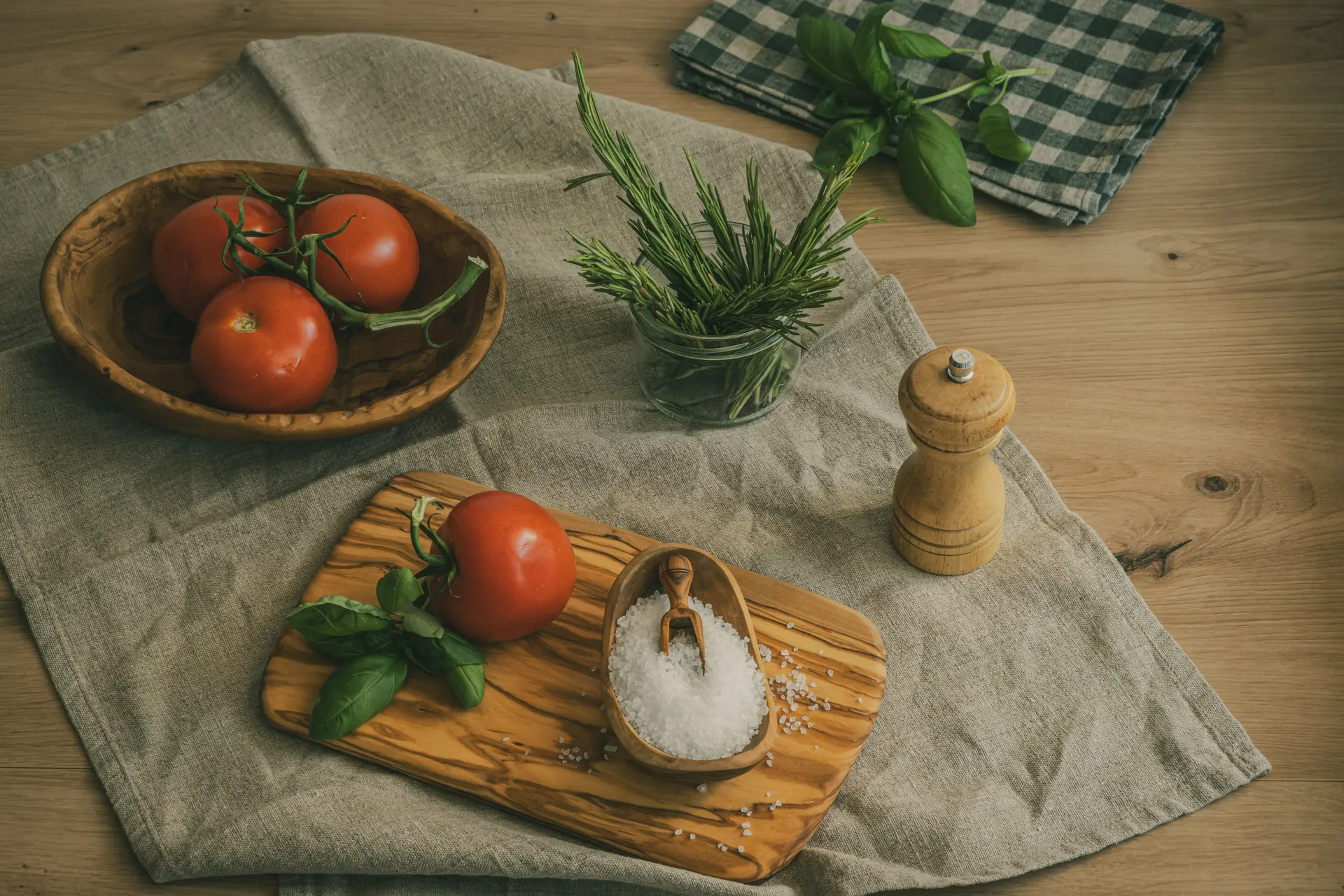 Coarse sea salt in an olive-wood bowl beside a board of tomato and basil on a linen-covered table