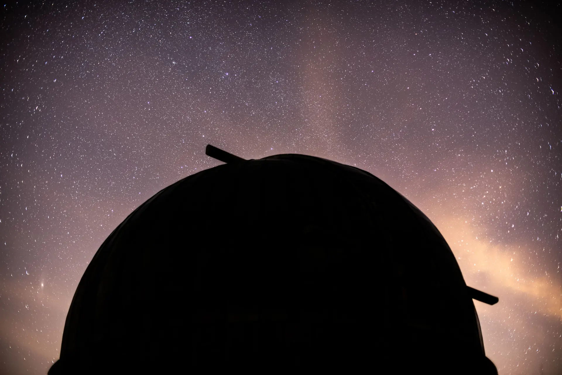 An observatory dome silhouetted black against a dense starfield with the Milky Way glowing at the right