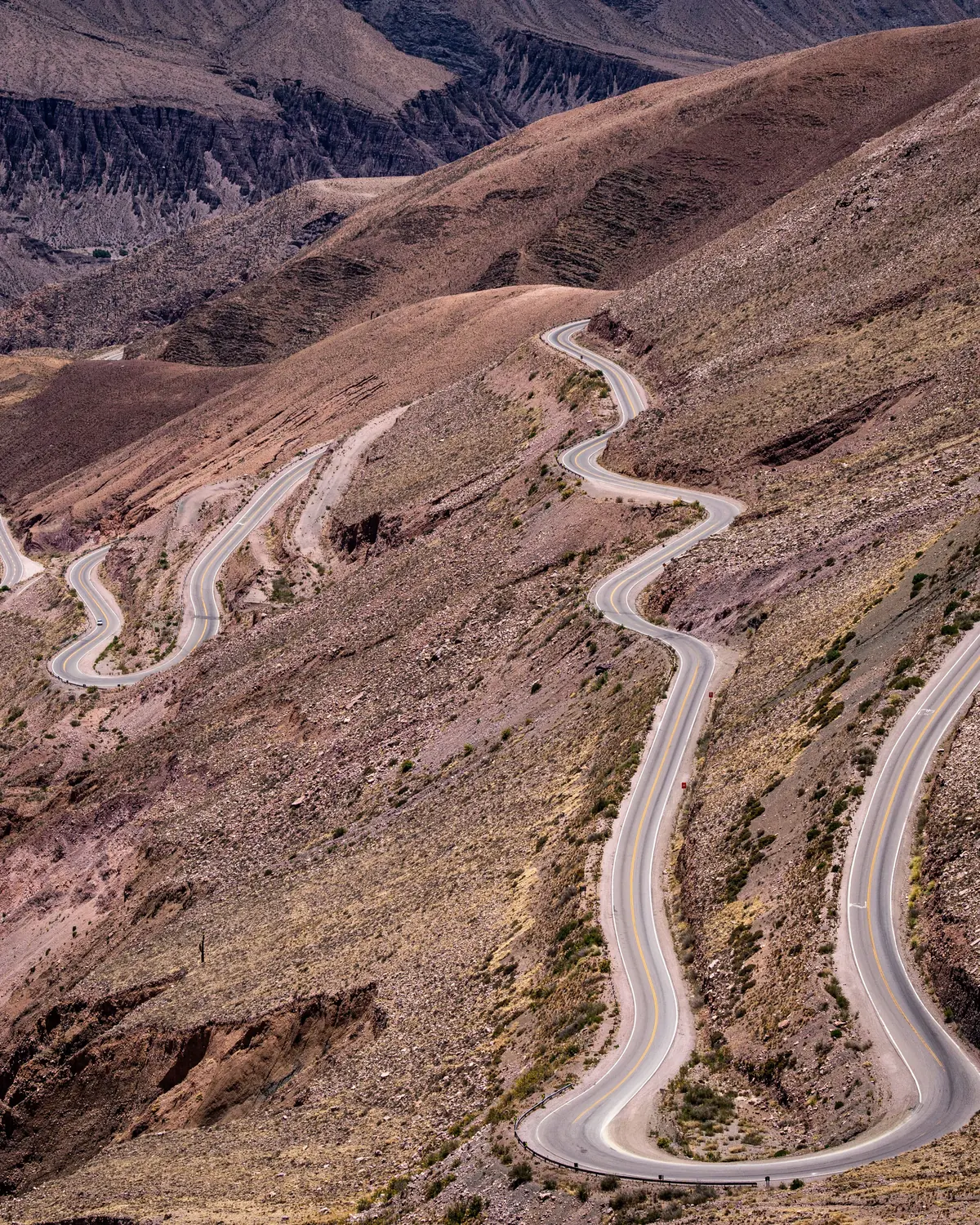 A road stacking switchback on switchback up a bare, rubble-strewn Andean slope toward the plateau rim
