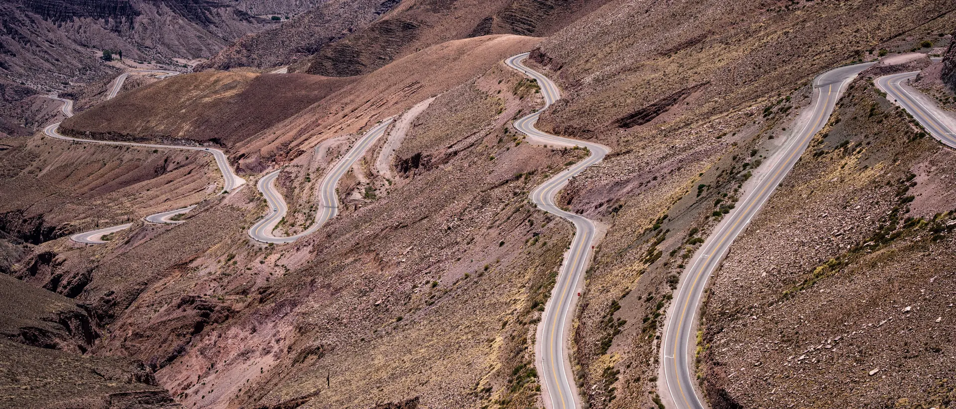 A road stacking switchback on switchback up a bare, rubble-strewn Andean slope toward the plateau rim