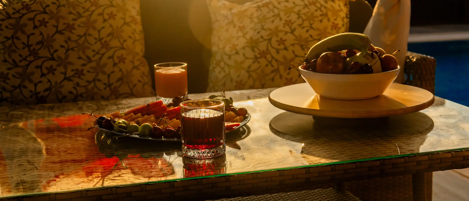 Two filled glasses, a dish of olives and a bowl of figs on a shaded terrace in low amber light