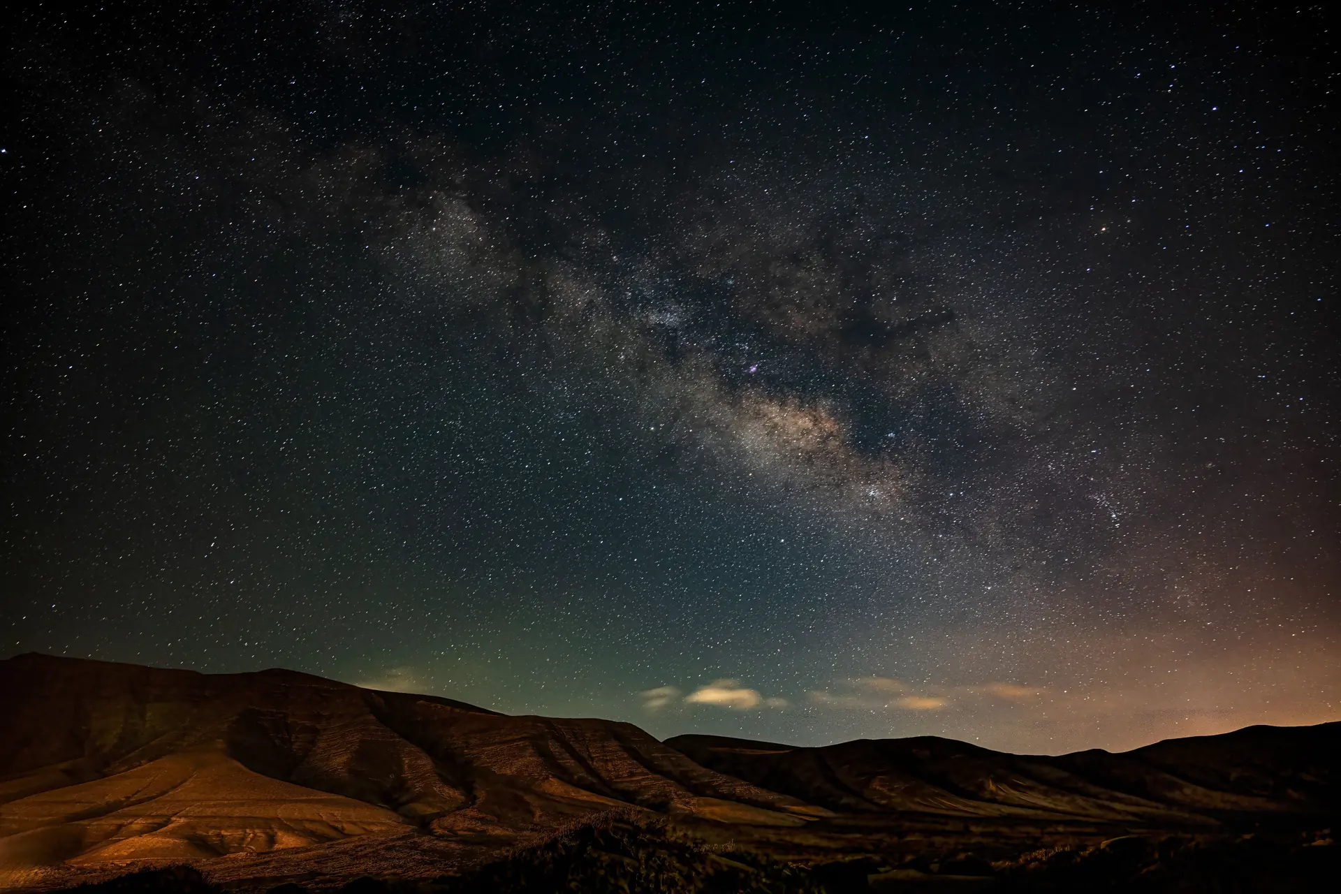 The Milky Way over a bare eroded desert ridge, a dense starfield with faint green airglow near the horizon